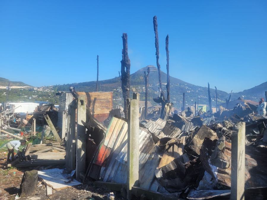 Collapsed shacks and charred posts below the mountain